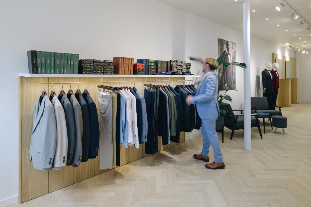 A person in a suit looking at a rack of clothes Description automatically generated